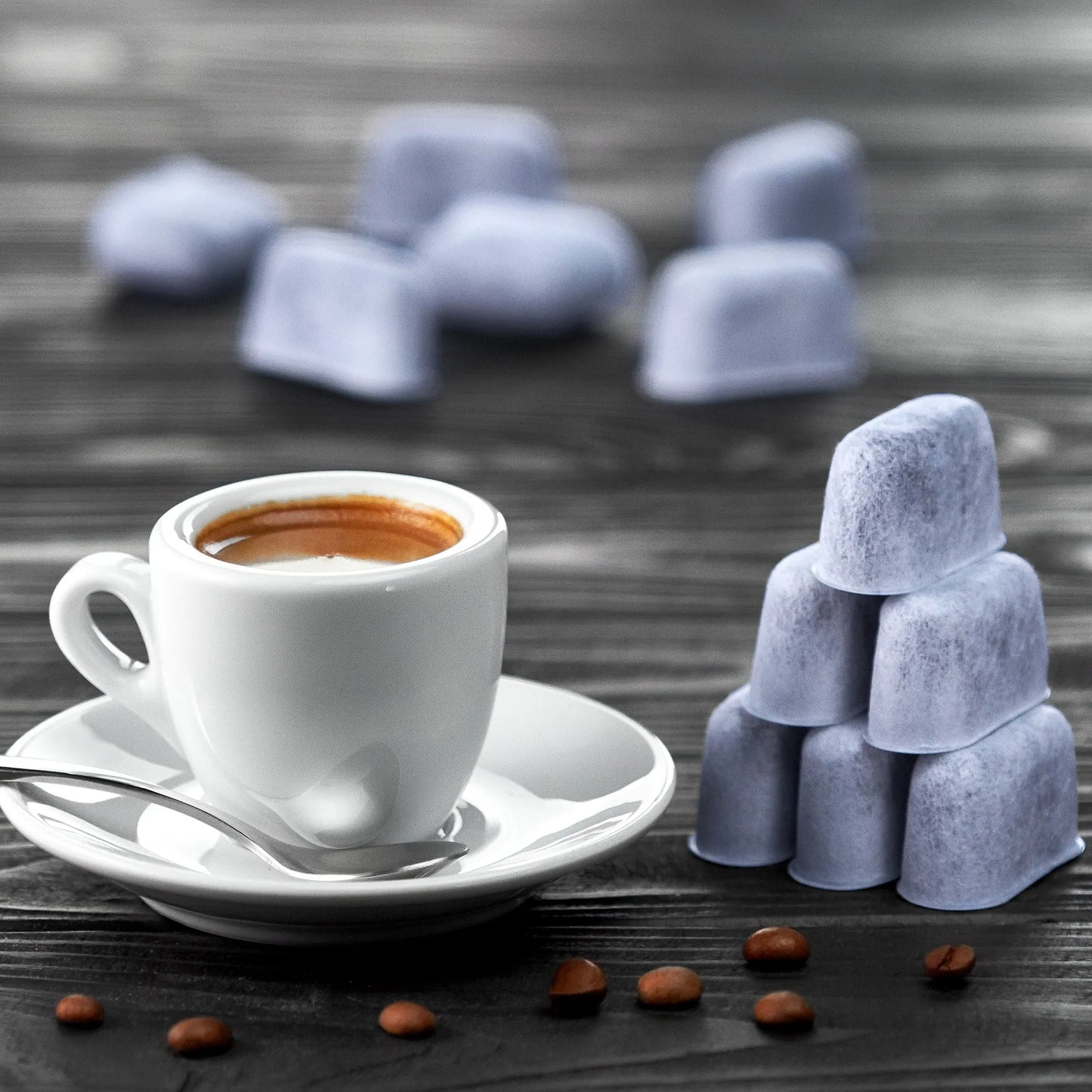 White coffee cup with saucer, spoon, and coffee beans on a wooden surface with stacked Cuisinart water filters