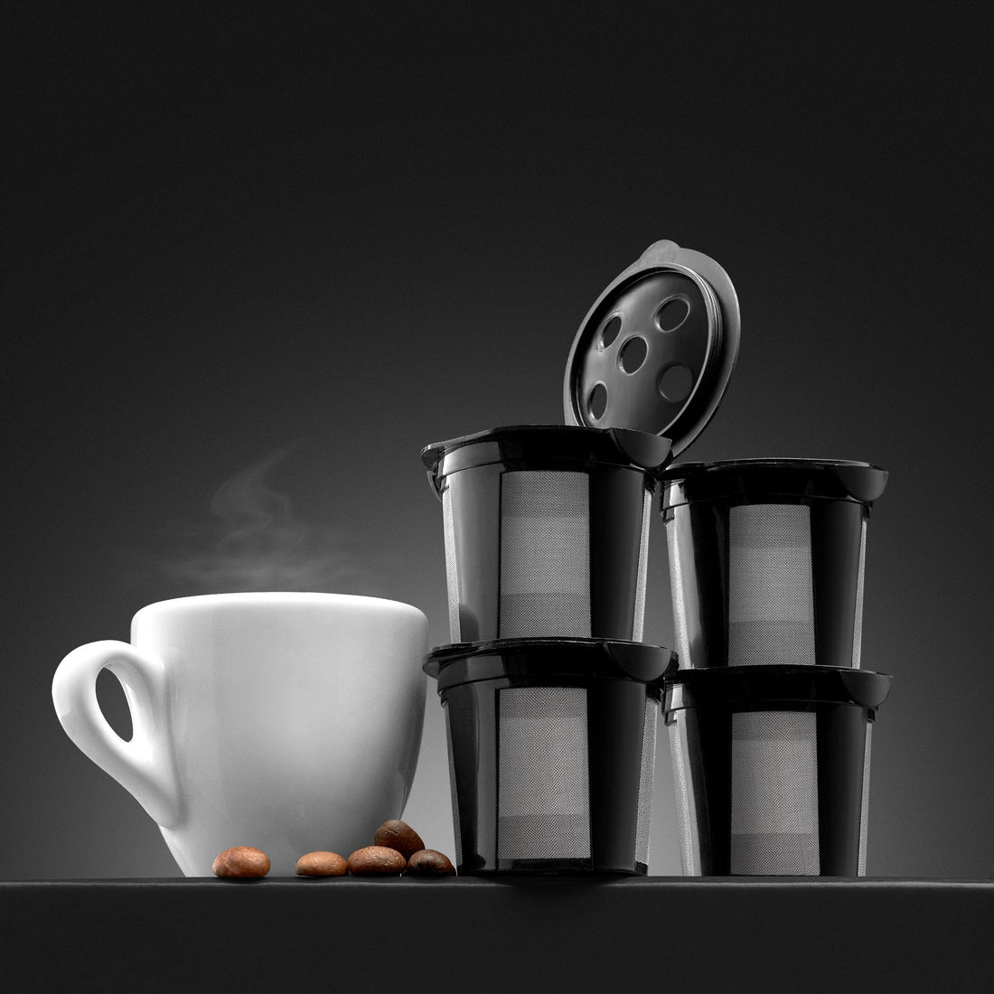 Stack of GoodCups reusable K-Cups with open lid showing five-needle holes, next to a white coffee mug and coffee beans