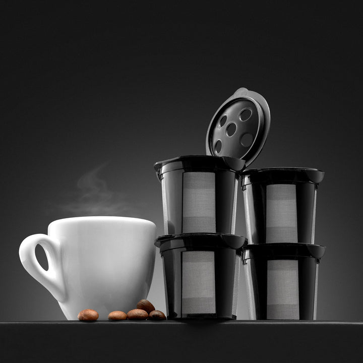 Stack of GoodCups reusable K-Cups with open lid showing five-needle holes, next to a white coffee mug and coffee beans