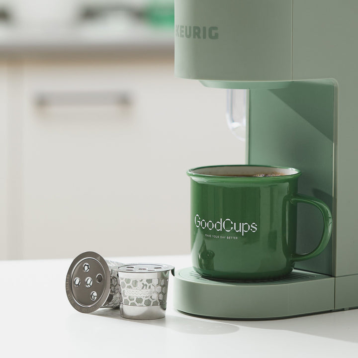 GoodCups stainless steel reusable K-Cups next to a Keurig coffee maker and GoodCups mug