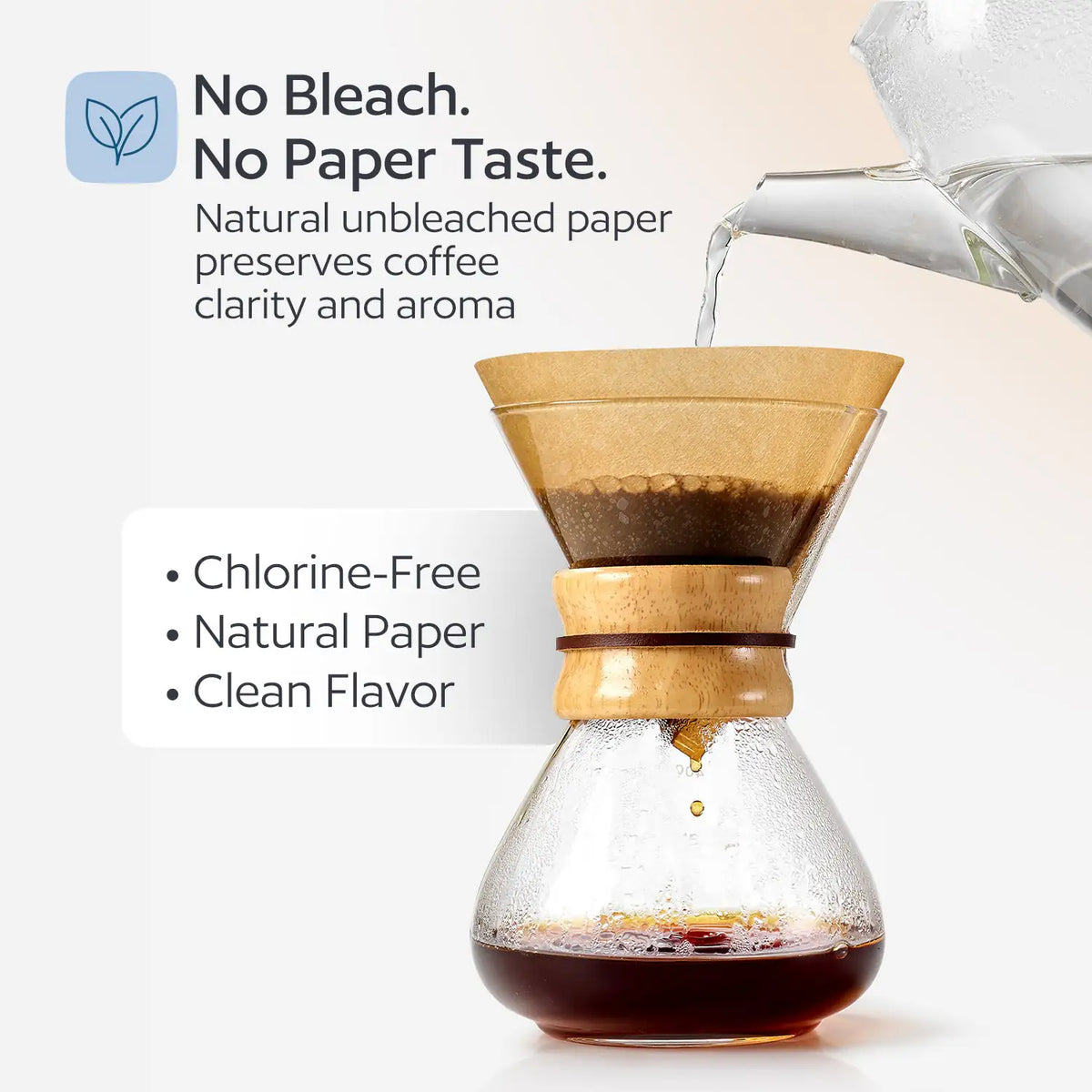 Unbleached cone coffee filter in a pour-over dripper with hot water being poured, brewing into a glass carafe on a wooden base