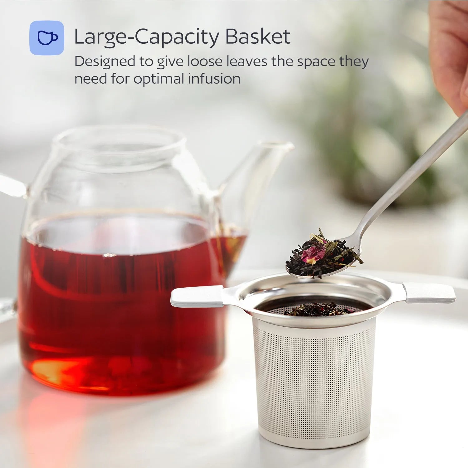 Tea infuser with loose tea leaves next to a teacup of red tea.