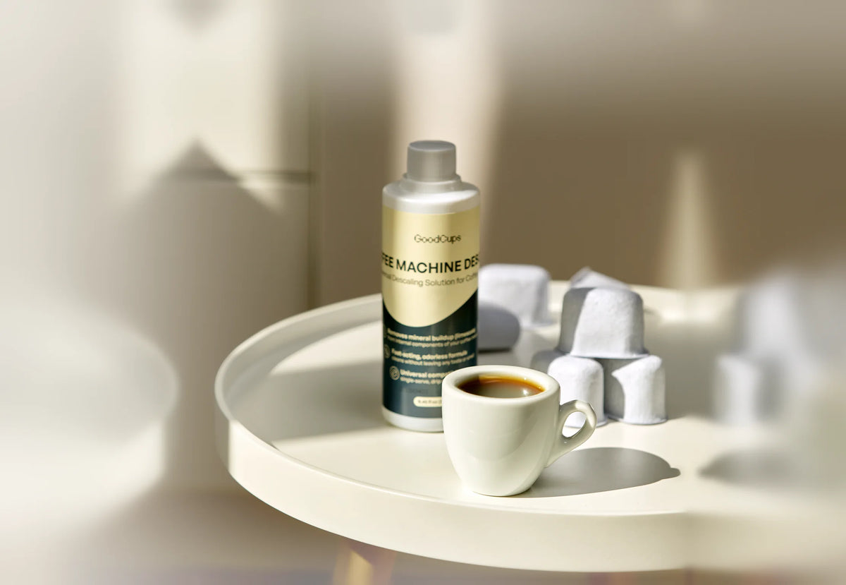 GoodCups Coffee Machine Descaler bottle with an espresso cup and water filters on a round table