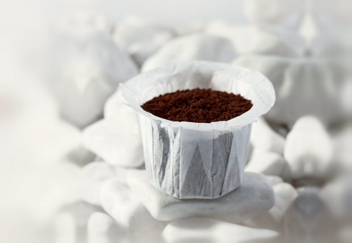Paper filter for reusable K-Cups filled with ground coffee on white stones
