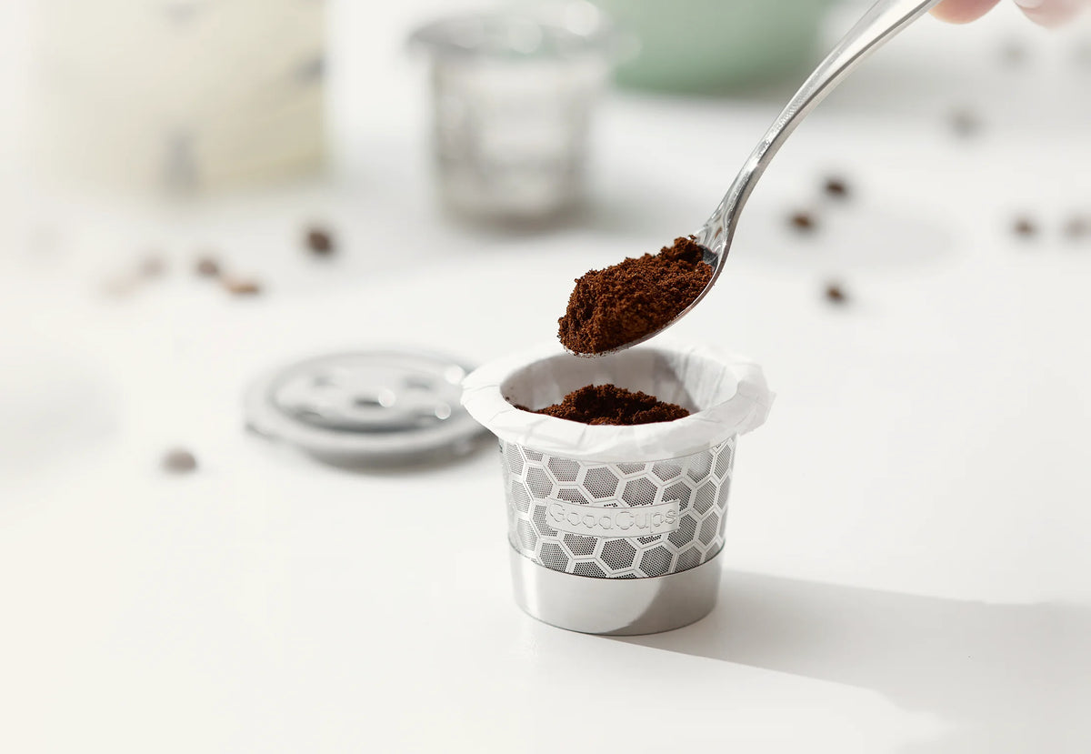 Spoon adding ground coffee into a GoodCups stainless steel reusable K-Cup lined with a paper filter